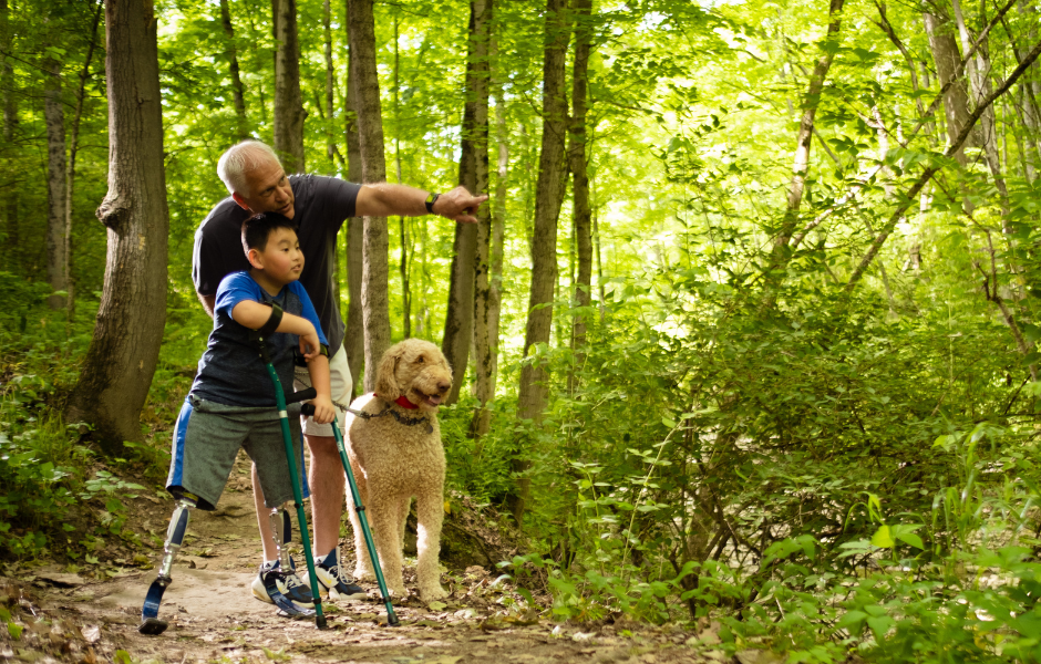 Child hiking with crutches and an elderly man with a dog.