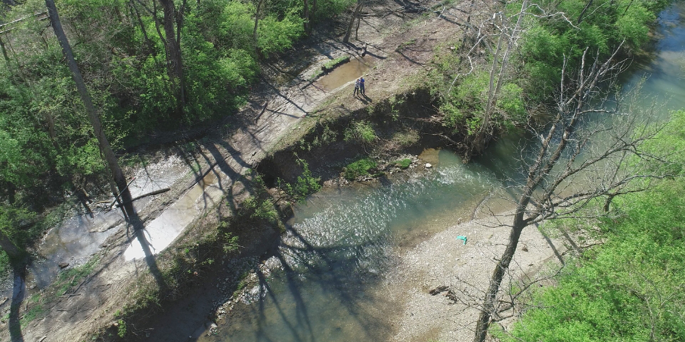 An aerial view of a creek eroding land above it, where a paved bike trail will be constructed